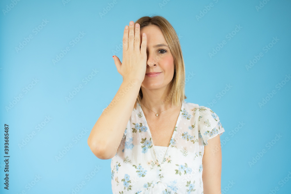 Portrait of beautiful woman covers her face by hand on blue background. Portrait of beautiful woman covers her face by hand on blue background.