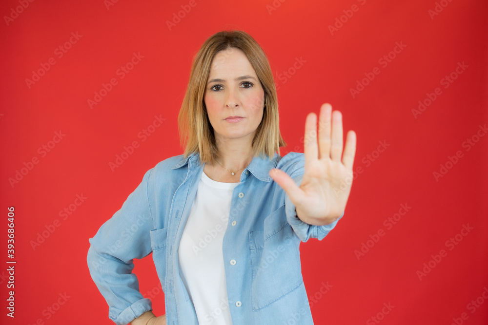 Portrait of a serious young woman standing with outstretched hand showing stop gesture isolated over red background Portrait of a serious young woman standing with outstretched hand showing stop gesture isolated over red background