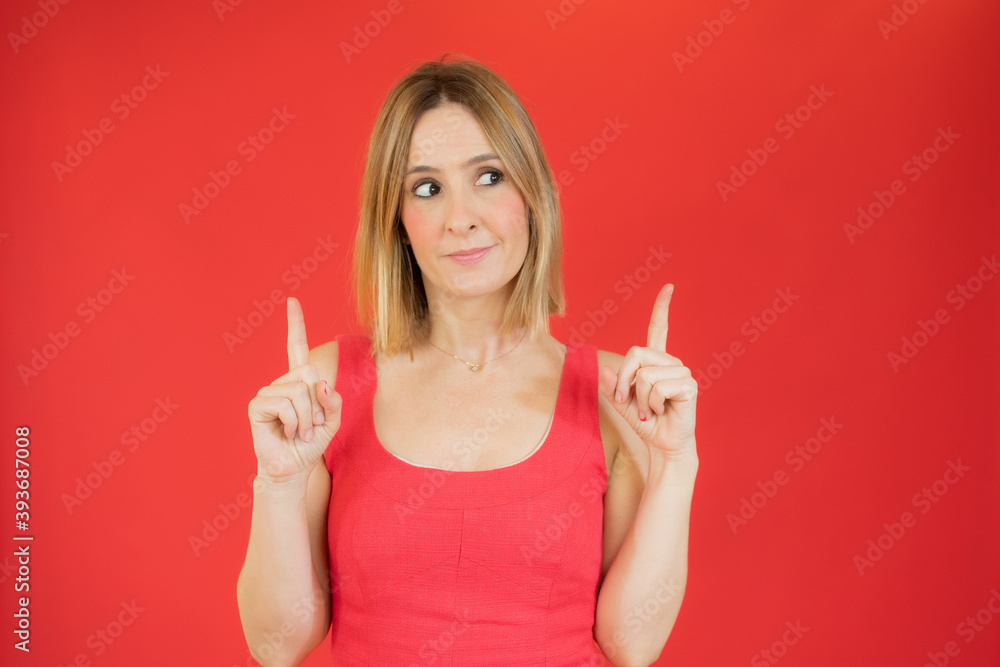 Portrait of a happy young woman dressed in red dress pointing fingers up at copy space isolated over red background Portrait of a happy young woman dressed in red dress pointing fingers up at copy space isolated over red background