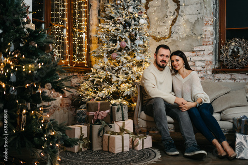 Portrait of a happy young family near a festive Christmas tree. The couple hugs each other tenderly. Good New Year spirit
