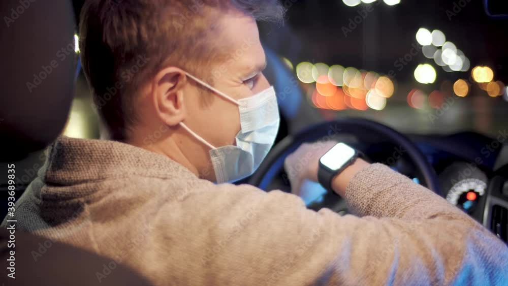 Young man with mask for protection from coronavirus checking smartwatch and ready for work, sitting in car, courier or freelancer work during covid-19 Young man with mask for protection from coronavirus checking smartwatch and ready for work, sitting in car, courier or freelancer work during covid-19