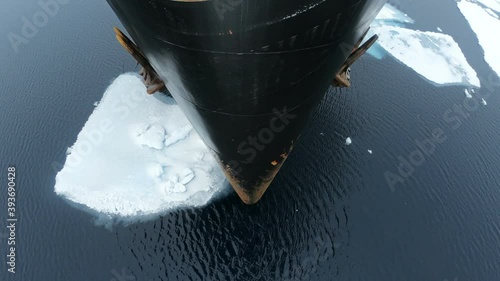 The bow of the ship flies over the water with ice. Chunks of ice on the water crack. The black prow of the ship with rust. Anchors hang on the sides