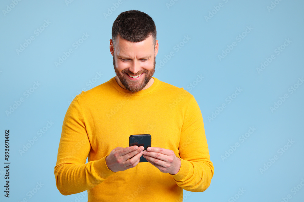 © JenkoAtaman - funny cheerful man in a yellow sweater with phone on blue background © JenkoAtaman - funny cheerful man in a yellow sweater with phone on blue background