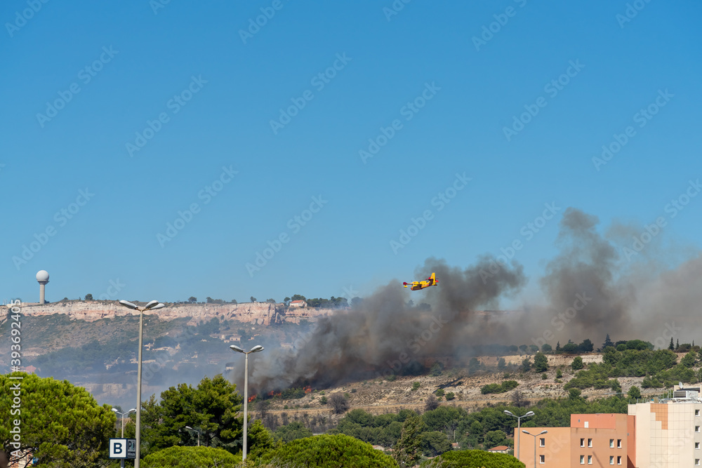 Fototapeta premium fire starts on the hills of Marseille, near Marignane airport. yellow fire-fighting plane is going to throwing water on it. 
