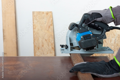 Carpenter cuts wood lath electric hand tool circular saw on desk, on background oriented strand board