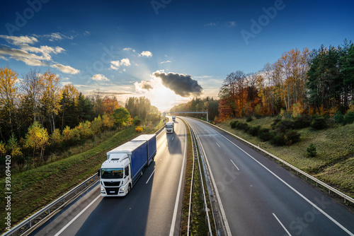 Obraz na płótnie Three trucks driving on the asphalt highway in autumn forested landscape at sunset w salonie