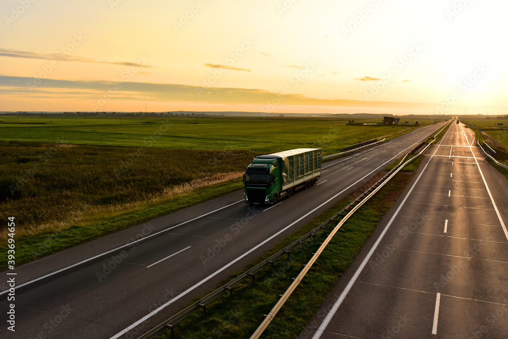 Truck with semi-trailer driving along highway on the sunset background. Out of focus, possible granularity, motion blur