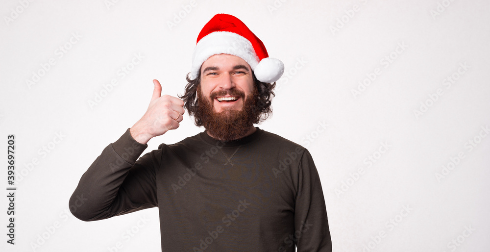 Cheerful bearded man wearing santa claus hat and showing thumb up Cheerful bearded man wearing santa claus hat and showing thumb up