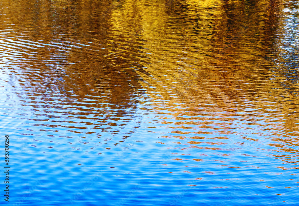 Beautiful, bright, picturesque, colorful, abstract yellow-blue background with yellow and broun autumn trees reflected in wavy blue water Beautiful, bright, picturesque, colorful, abstract yellow-blue background with yellow and broun autumn trees reflected in wavy blue water