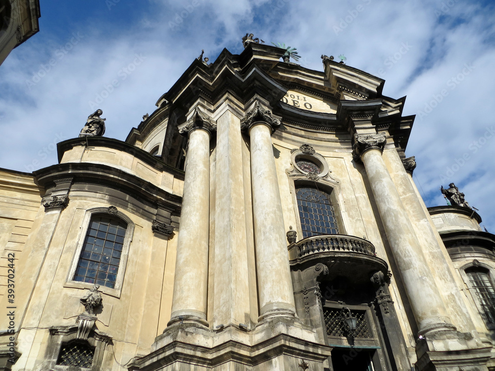 Facade of the building of the cathedral and the monastery with columns and figures on the roof against the background of a blue sky with clouds. Dominican Church Facade of the building of the cathedral and the monastery with columns and figures on the roof against the background of a blue sky with clouds. Dominican Church