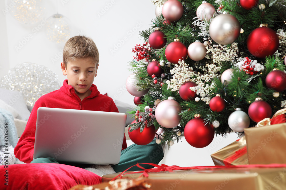merry christmas and happy holidays, child stay at home with computer near the illuminated and decorated tree and wrapped gift packages