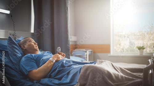 Medical Hospital Ward  Beautiful Chinese Man is Resting on a Bed. Recovering after Successful Surgery. Male Patient Sleeping and Gettin Well. Modern High Tech Equipped Room with Warm Sun LIght.