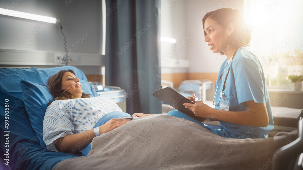 Obraz premium Hospital Ward: Friendly Hispanic Head Nurse Fills Medical History Form, Talks to Female Patient Recovering in Bed. Professional Nurse Helps Happy Woman Get Better after Surgery. Shot with Sun Flare.