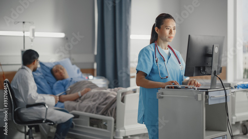 Fotografia Hospital Ward: Professional Experienced Chinese Head Nurse / Doctor Uses Medical Computer Checking Medical Data