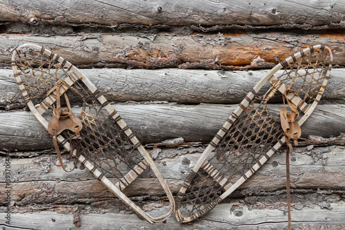Unused and neglected snowshoes hang on the weathered sides of an abandoned Trappers Cabin in the Northwest Territories of Canada