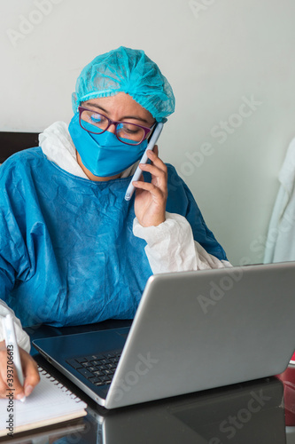 A young, serious doctor in a blue uniform and medical mask working on a laptop, sitting at a clinic desk