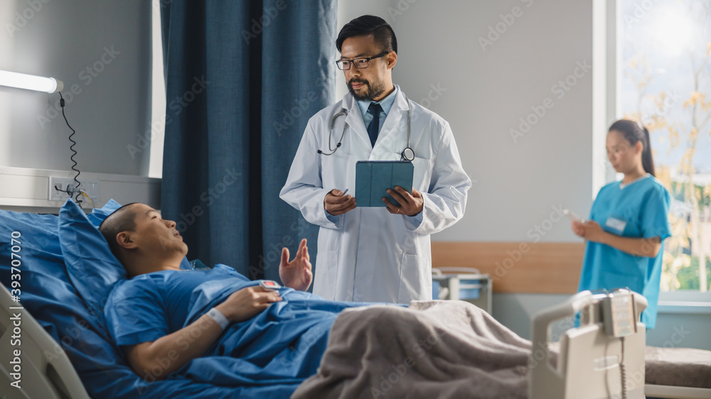 Hospital Ward: Friendly Chinese Doctor Talks to Handsome Male Patient Resting in Bed, Uses Tablet Computer, Explains Test Results. Physician Talks to Man Recovering after Successful Surgery Hospital Ward: Friendly Chinese Doctor Talks to Handsome Male Patient Resting in Bed, Uses Tablet Computer, Explains Test Results. Physician Talks to Man Recovering after Successful Surgery