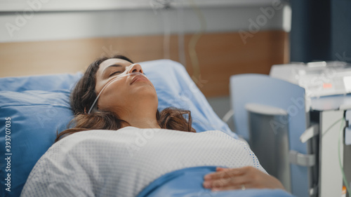 Medical Hospital Ward: Beautiful Latin Woman with Nasal Cannula is Resting on a Bed. Recovering after Successful Surgery Female Patient Sleeping and Gettin Well. Modern High Tech Equipped Room photo