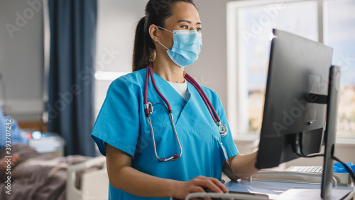 Hospital Ward: Close-up Portrait Shot of a Professional Experienced Chinese Head Nurse / Doctor Wearing Face Mask Uses Medical Touch Screen Computer, Checking Patient's Medical Data, Treatment Plan.