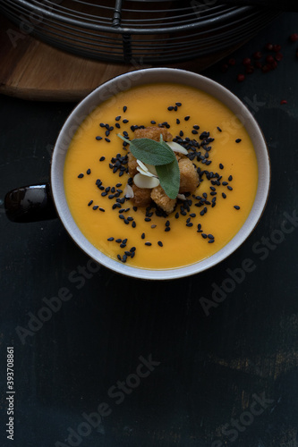 Closeup view of a delicious carrot and pumpkin cream soup in a bowl with some leaves of sage at the top. A copy space is at the bottom.