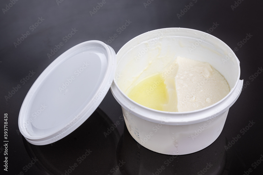 Layer of whey protein formed on top of packaged yogurt after opening in dark background. Layer of whey protein formed on top of packaged yogurt after opening in dark background.