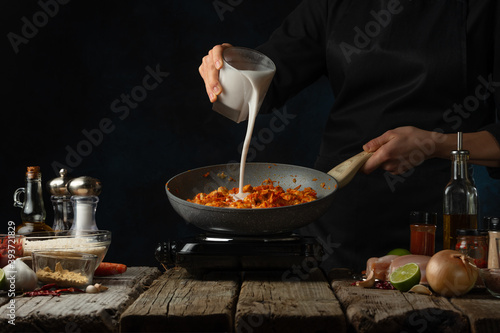 Fotografie Professional chef pours milk into pan with chicken fillet