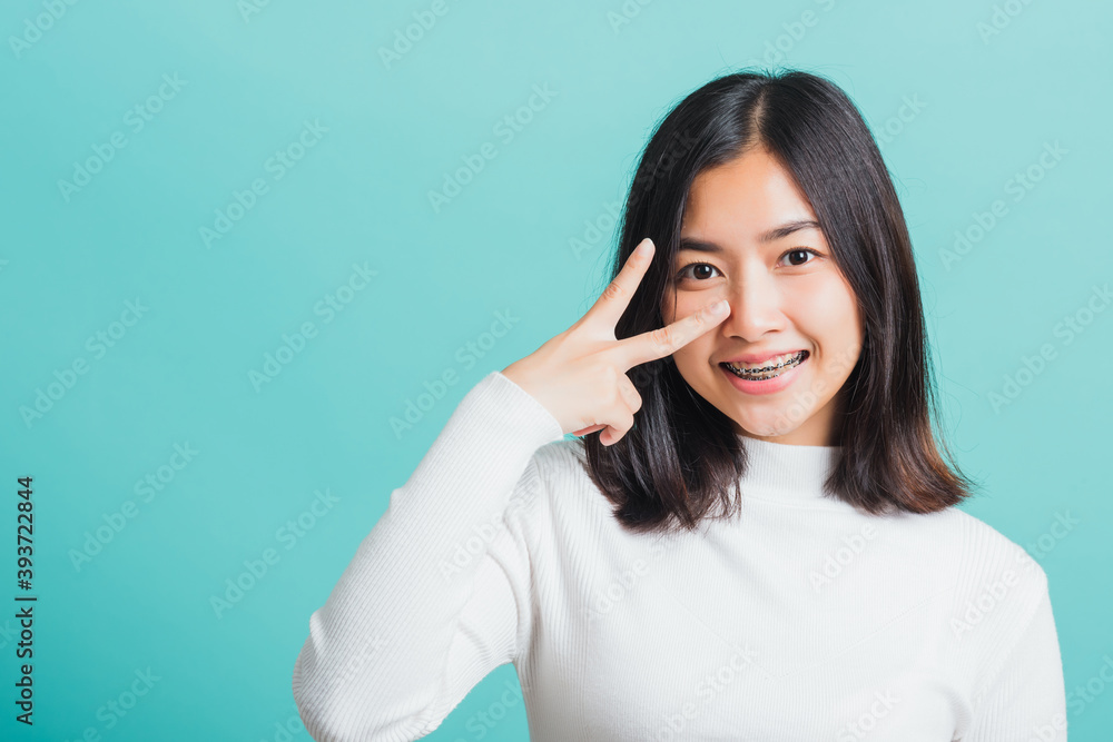Portrait female give V-sign near-eye make Hollywood white smile, Young beautiful Asian woman showing peace gesture victory, studio shot isolated on a blue background Portrait female give V-sign near-eye make Hollywood white smile, Young beautiful Asian woman showing peace gesture victory, studio shot isolated on a blue background