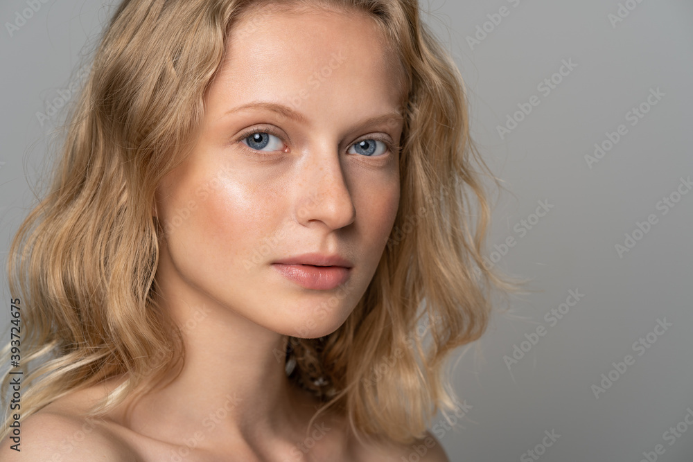 Close up of young woman face with blue eyes, curly natural blonde hair and eyebrows, has no makeup, looking at camera. Girl with perfect fresh clean skin over studio grey background. Youth concept. Close up of young woman face with blue eyes, curly natural blonde hair and eyebrows, has no makeup, looking at camera. Girl with perfect fresh clean skin over studio grey background. Youth concept.