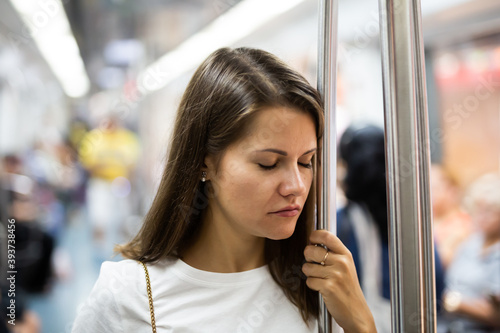 Tired young woman sleeps standing in subway car