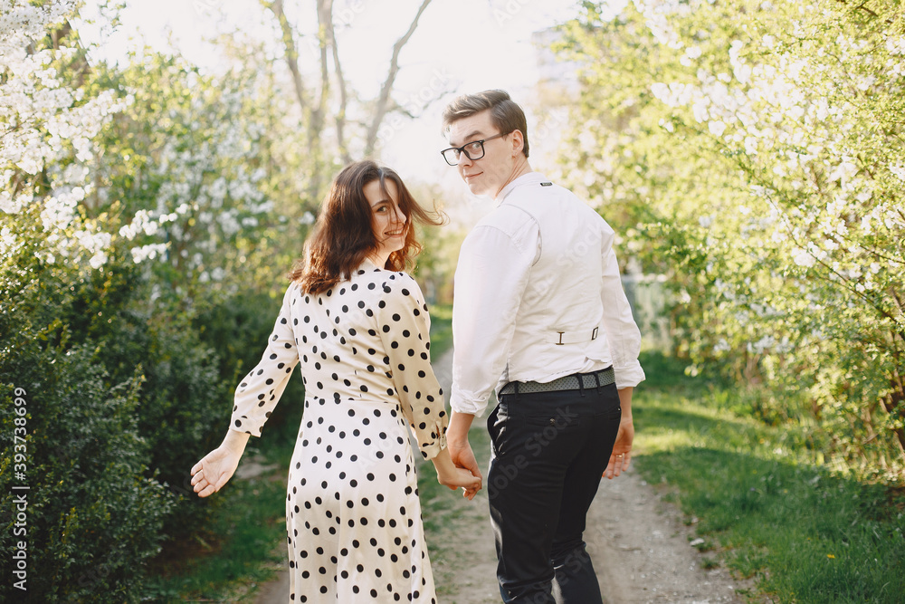 Fototapeta premium Man and woman in blooming garden on spring day. Couple in love spend time in spring garden. Flowers on background.