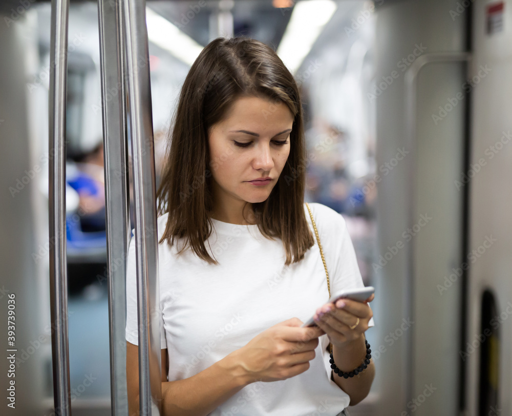 Portrait of young smiling woman using phone standing in subway car