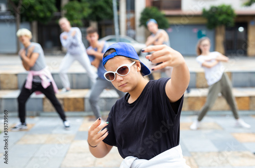 Confident teen b-girl dancing with group of friends on city street. Urban lifestyle. Hip-hop generation.