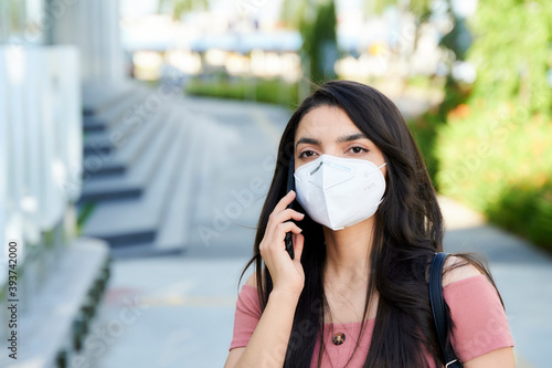 portrait of beautiful young woman wearing face mask using smart phone in the street