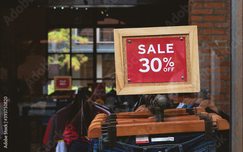 A business clothing store sign hangs a sale sign on the door and shows the status of the store with a blurred background.