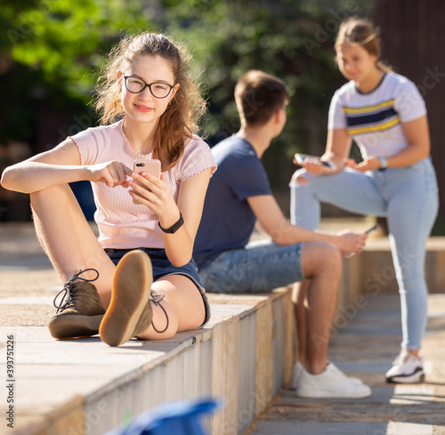 Teen girl is passionate about playing on smartphone while friends are sitting nearby