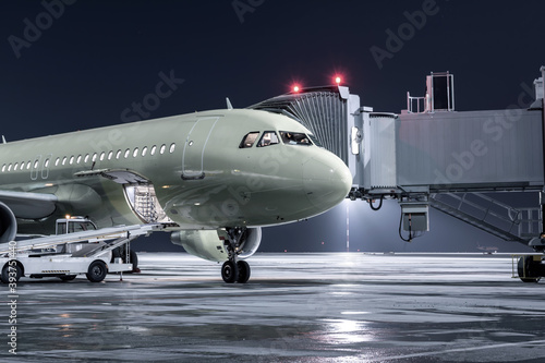 The passenger airplane stands at the jetway on an airport night apron. The baggage compartment of the aircraft is open and the luggage is being loaded
