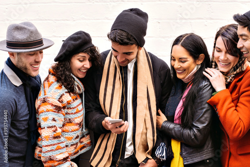Картината върху платно Group of young adults convene over a smart phone - Winter wear - Seasonal - Fun