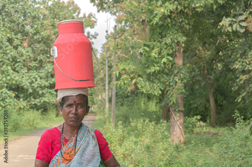 Photography Beautiful photo of an empowered tribal Indian woman in ethnic attire, carrying and balancing milk vessel on her head to deliver it door to door for her customers