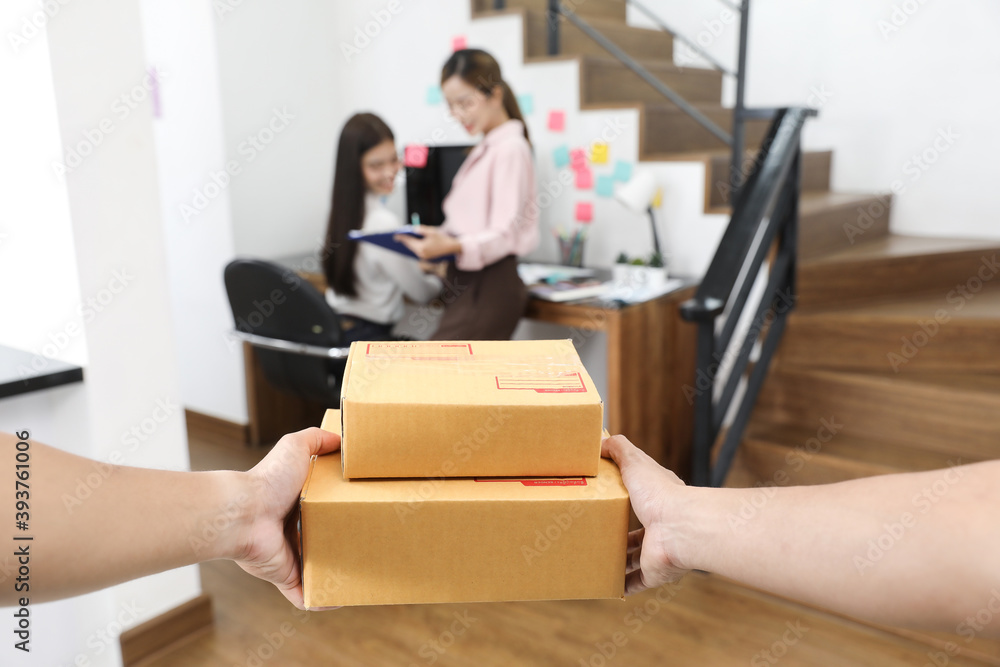Delivery personnel in red uniform delivering packages of goods to home with a smile and happy face. Young Asian business receiving boxes from the postman at the home office. Selective focus on hand