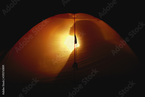 Silhouette of a woman in a tent at night. Female silhouette through the walls of a transparent orange tent at night in the mountains.