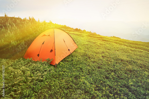 View of an orange tent in the summer in mountain forest.