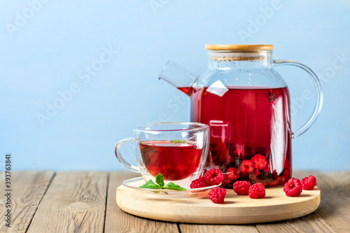 Herbal tea with berries, raspberries, mint leaves and hibiscus flowers in glass teapot and cup on wooden table Medicine for cold Vitamin drink Rustic style