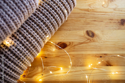 The stack of sweater lies on a wooden table with garland. Space for text