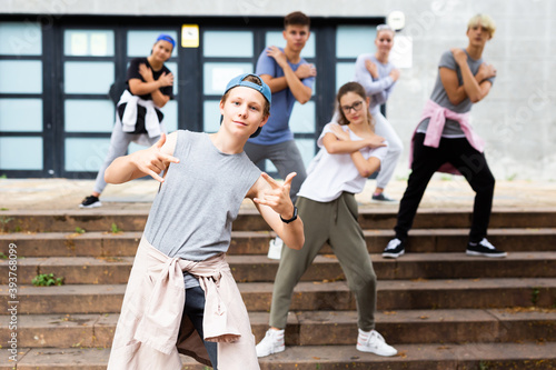 Positive teen boy dancing modern street dance outdoors with teenagers in background.