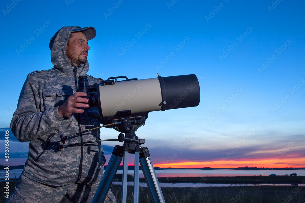 A male astronomer observes the sky through a telescope. Amateur astronomy concept.