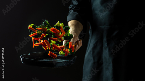 Chef cooking vegetables on a pan. flying vegetables scattering in a freeze motion of a cloud midair on black