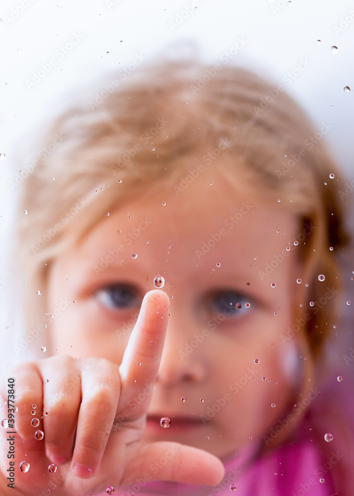 The little girl touching the wet glass
