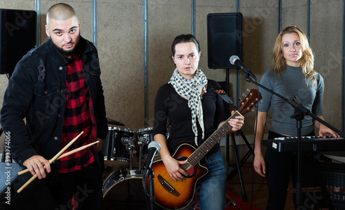 expressive excited young group of rock musicians posing with instruments in recording studio