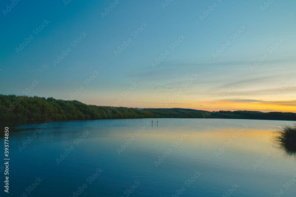 Fototapeta premium Calm peaceful lake sunset with colorful sky on background and smooth reflection on water