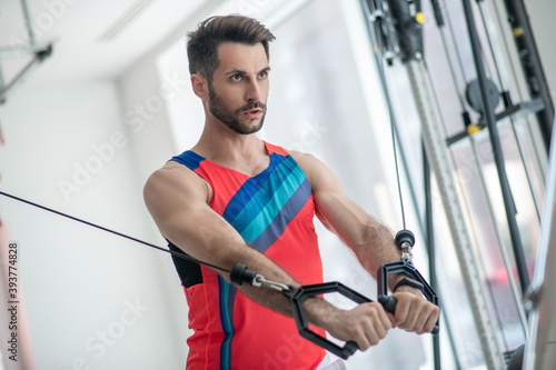 Dark-haired man working on his arms in the gym and looking concentrated